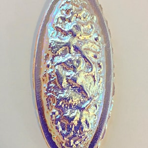 May include: An iridescent oval glass button with a raised design of a floral pattern. The button has a purple, blue, and gold iridescent finish.