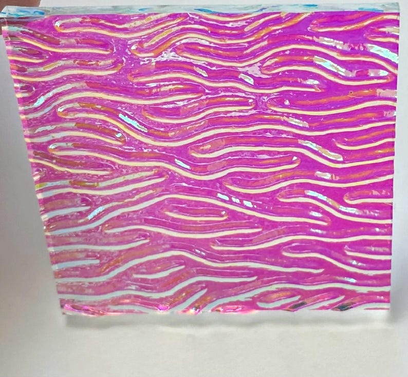 May include: A rectangular piece of iridescent material with a wavy pattern. The colors shift from pink to purple with white and yellow highlights, creating a shimmering effect. The material appears to be translucent.
