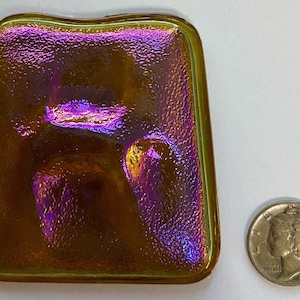 May include: A small, iridescent, rectangular glass tile with a textured surface. The tile is a deep gold color with hints of purple and green.