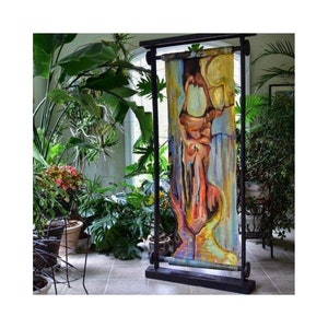 May include: A colorful abstract painting on canvas is mounted on a wooden frame with black metal rollers. The painting is displayed in a room with plants.