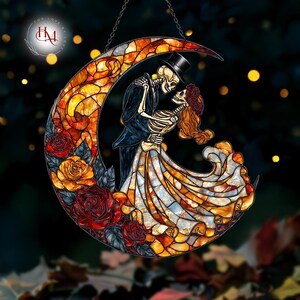 Pode incluir: Lua crescente em vitral com um casal de esqueletos abra&ccedil;ados. A mulher usa uma coroa de flores, o homem uma cartola. A lua &eacute; preenchida com cores quentes e rodeada de rosas. Pendurado por uma corrente.