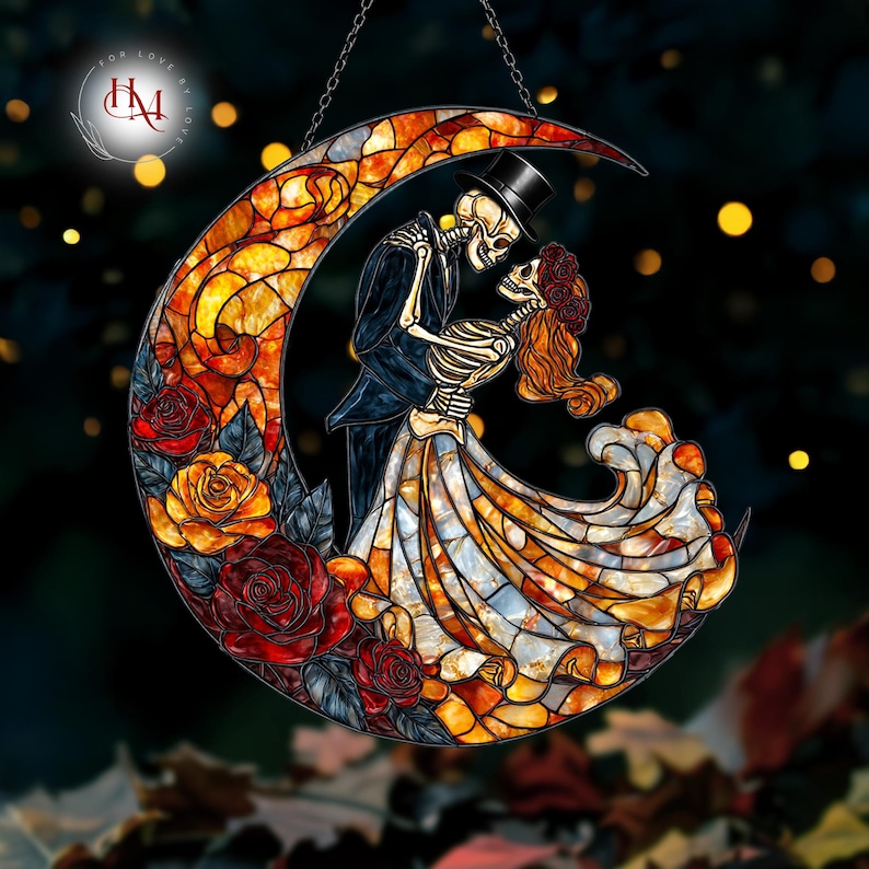 Pode incluir: Lua crescente em vitral com um casal de esqueletos abra&ccedil;ados. A mulher usa uma coroa de flores, o homem uma cartola. A lua &eacute; preenchida com cores quentes e rodeada de rosas. Pendurado por uma corrente.