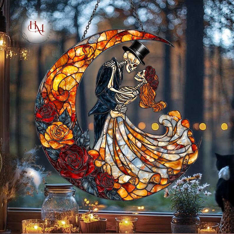 Pode incluir: Vitral em forma de lua crescente com um casal de esqueletos em trajes formais, abra&ccedil;ando-se. A lua &eacute; decorada com rosas vermelhas e laranja. A obra de arte &eacute; suspensa por uma corrente, com um fundo desfocado de &aacute;rvores e luzes.
