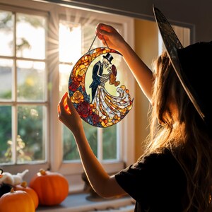 Pode incluir: Decora&ccedil;&atilde;o de meia-lua em vitral com um casal de esqueletos em trajes formais, rodeados por rosas. A obra de arte &eacute; sustentada por uma corrente, com um fundo quente e ensolarado. Um item de decora&ccedil;&atilde;o para casa com tema de Halloween ou g&oacute;tico.