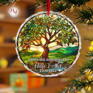 Könnte beinhalten: Runder Schmuckanhänger im Glasmalerei-Stil mit einem Baumdesign. Der Baum hat einen braunen Stamm und grüne Blätter, vor einer gelb-grünen Landschaft. Der Text lautet "HAPPY 3RD ANNIVERSARY" und die Namen "Chloe & Alex" mit dem Datum "23.10.2022".