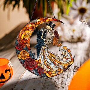 Pode incluir: Decora&ccedil;&atilde;o de Halloween em vitral com um casal de esqueletos dan&ccedil;ando dentro de uma lua crescente. A lua &eacute; decorada com rosas vermelhas e amarelas. Os esqueletos est&atilde;o vestidos com roupas formais. Uma corrente preta est&aacute; presa para pendurar.