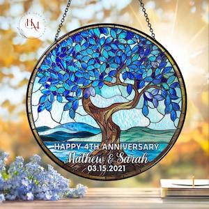 May include: A round stained glass window featuring a tree with blue leaves and a brown trunk. The window has a black border and includes the text "HAPPY 4TH ANNIVERSARY Mathew & Sarah 03.15.2021". The window is hanging from a chain.