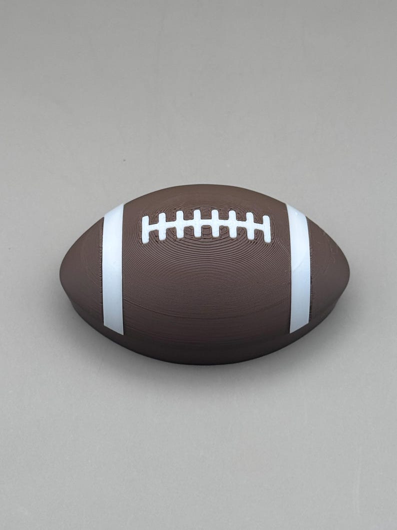 May include: A brown football with white stripes and laces. The football is oval-shaped and has a textured surface. The white stripes run along the sides, and the white laces are in the center.