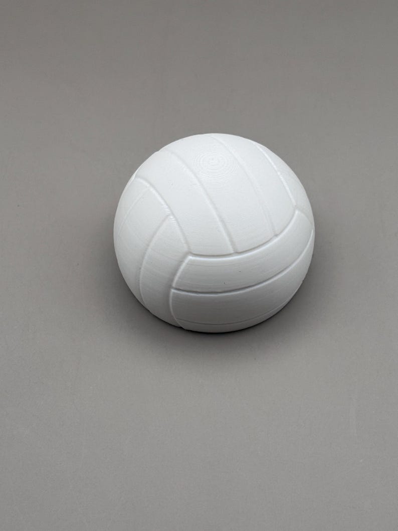 May include: A white volleyball with a textured surface. The ball has a classic panel design with curved seams. The ball is a solid color and appears to be made of a durable material.