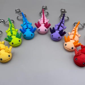 May include: A collection of colorful axolotl keychains in various shades, including yellow, green, blue, pink, purple, orange, and red. Each keychain features a detailed axolotl design with a silver-tone clasp.