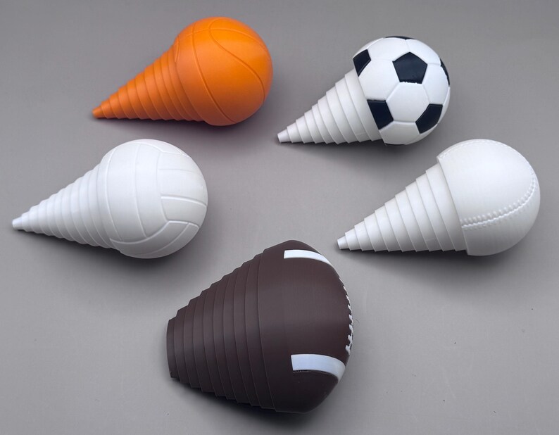 May include: Five sports-themed bottle stoppers. The stoppers are shaped like a basketball, soccer ball, volleyball, baseball, and football. The basketball stopper is orange, the soccer ball is black and white, the volleyball and baseball are white, and the football is brown.