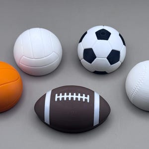 May include: An assortment of sports balls, including a basketball, volleyball, soccer ball, baseball, and football. The basketball is orange, the volleyball and baseball are white, the soccer ball is black and white, and the football is brown with white stripes.