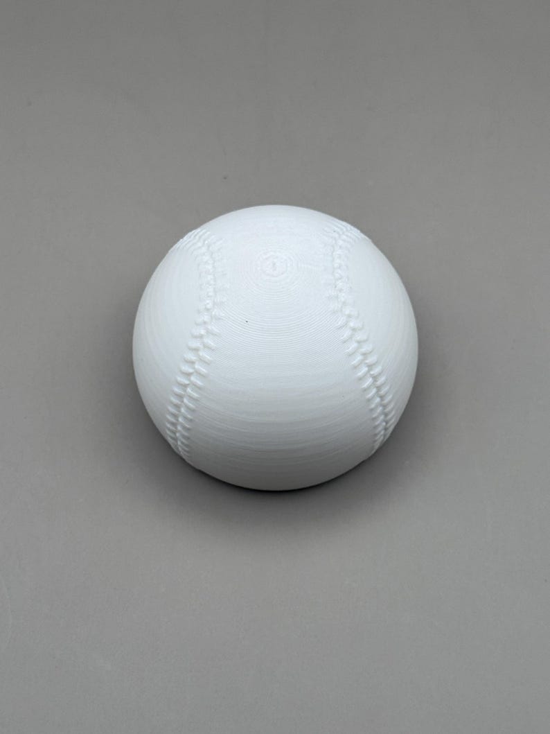 May include: A white baseball with red stitching details. The ball is centered on a gray background. The baseball is a classic sports item.