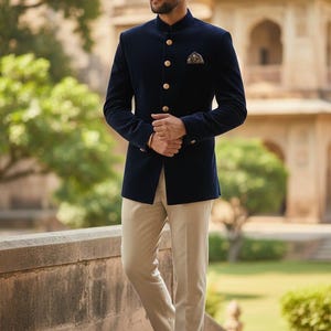 Op de afbeelding: Een marineblauwe fluwelen jasje met gouden knopen en een opstaande kraag wordt gecombineerd met een kaki broek. Een pochet voegt een vleugje detail toe. De outfit wordt gecompleteerd met bruine leren schoenen. Geschikt voor formele gelegenheden.