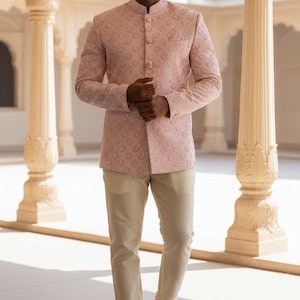 Peut inclure: Veste bandhgala rose clair brodée avec un col mao, associée à un pantalon beige et des chaussures en cuir marron. La veste présente un motif subtil et répétitif. La tenue est adaptée aux occasions formelles.