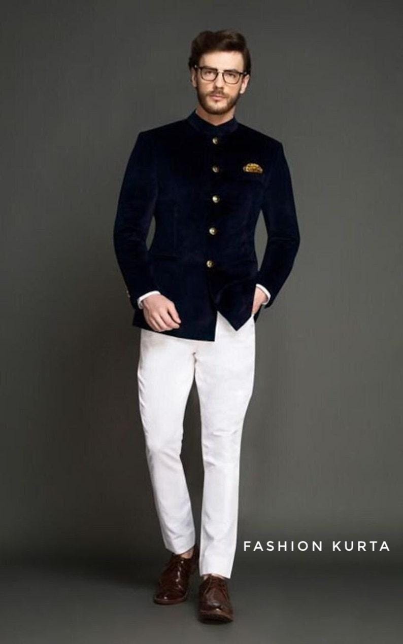 May include: A navy blue velvet jacket with gold buttons and a mandarin collar is paired with white pants and brown shoes. The outfit is completed with a pocket square. The text "FASHION KURTA" is visible.