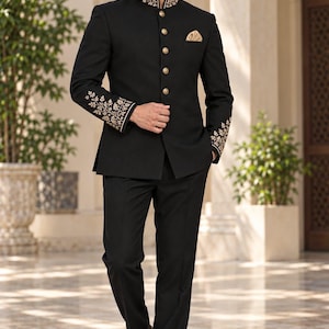 Könnte beinhalten: Ein schwarzer Bandhgala-Anzug mit Stehkragen, goldener Stickerei, goldenen Knöpfen und passender goldener Blumenstickerei an den Ärmelbündchen. Das Set besteht aus einer schwarzen Jacke mit goldenem Einstecktuch und einer schwarzen Hose.