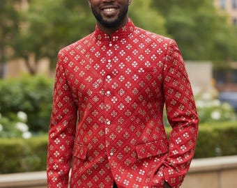 May include: A red patterned blazer with a mandarin collar and white buttons. The blazer features a repeating gold and white floral design. The person is wearing black pants and has their hand in their pocket.