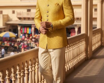 May include: A man wearing a yellow patterned jacket with matching buttons, a pocket square, and cream-colored pants. The jacket has a mandarin collar. He is wearing gold-colored shoes. The background shows a building with arches.