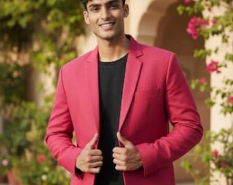 May include: A magenta blazer with a black t-shirt and black pants. The blazer is a solid color and has a classic two-button design. The person is smiling and standing in front of a background of flowers and plants.