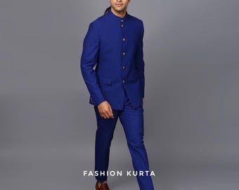 May include: A cobalt blue suit with a mandarin collar jacket and matching trousers. The jacket features gold-colored buttons. The text "FASHION KURTA" is printed at the bottom. The person is wearing brown leather shoes.