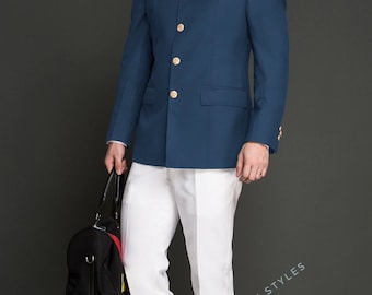 May include: A man in a blue suit with gold buttons, a red pocket square, and white pants. He is wearing sunglasses and holding a black duffel bag. The text "KINGSMAN SUIT STYLES" is visible on the pants.