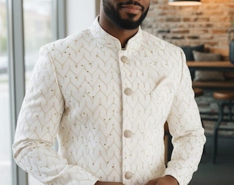 May include: Ivory-colored jacket with a mandarin collar and a subtle, repeating gold pattern. The jacket features three large, decorative buttons and a pocket on the chest. The sleeves are long, and the jacket is worn over a dark shirt.