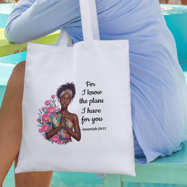 May include: White tote bag featuring an illustration of a woman with a floral design and the text "For I know the plans I have for you - Jeremiah 29:11". The bag has white handles and is made of a sturdy fabric.