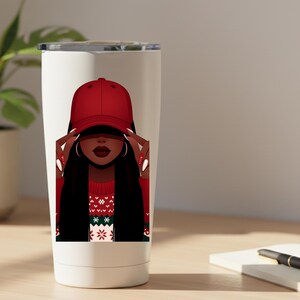 May include: A white tumbler featuring a graphic of a person wearing a red baseball cap, with long black hair and a red sweater with a Christmas pattern. The person is holding the cap with their hands.