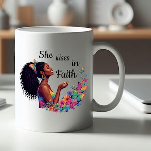 May include: White ceramic mug featuring a colorful illustration of a woman with curly black hair, butterflies, and flowers. The mug has the text "She rises in Faith". The handle is on the right side.