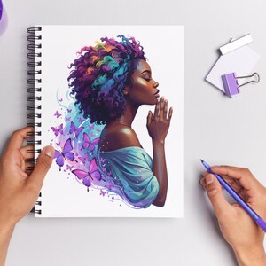 May include: Spiral-bound notebook featuring an illustration of a woman with colorful hair and butterflies. The artwork depicts a woman with her hands clasped in prayer, surrounded by purple butterflies and a blue aura.
