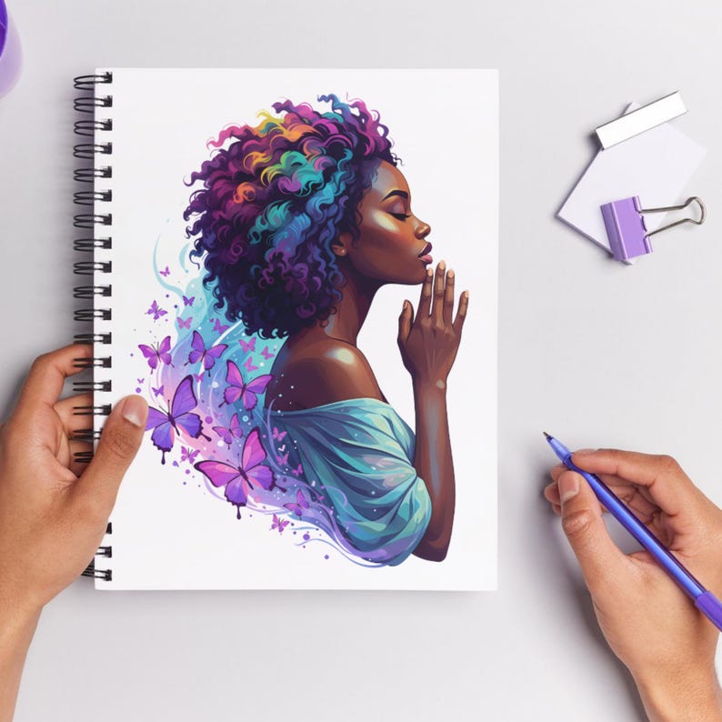 May include: Spiral-bound notebook featuring an illustration of a woman with colorful hair and butterflies. The artwork depicts a woman with her hands clasped in prayer, surrounded by purple butterflies and a blue aura.