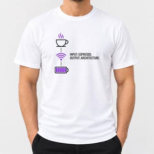 May include: A white short-sleeved t-shirt featuring a graphic with a coffee cup, a purple Wi-Fi symbol, and a purple battery icon. The text reads: INPUT: ESPRESSO. OUTPUT: ARCHITECTURE. The design is centred on the chest of the garment.
