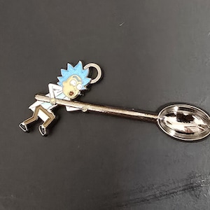 May include: A silver spoon with a cartoon character of Rick Sanchez from the animated series Rick and Morty. The character is holding onto the spoon and has a blue and white design.