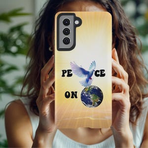 Könnte beinhalten: Eine Handyhülle mit gelb-orangefarbenem Farbverlauf im Hintergrund. Die Hülle zeigt eine blau-weiße Taube über einem Globus mit den schwarzen Worten "PEACE ON". Die Handyhülle wird vor einer Person gehalten.
