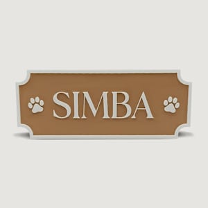 Peut inclure: Panneau de nom pour animal de compagnie rectangulaire marron avec bordure blanche. Le nom "SIMBA" est écrit en lettres majuscules blanches, avec des empreintes de pattes de chaque côté.