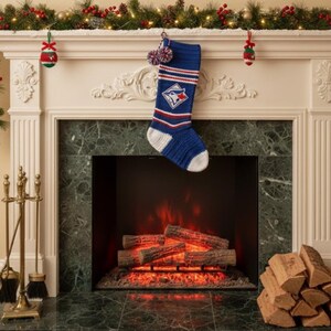 Può includere: Una calza di Natale lavorata a maglia blu e bianca con il logo dei Toronto Blue Jays è appesa sopra un camino. Il camino ha una cornice in marmo verde e una ghirlanda decorativa. Una pila di legna da ardere si trova a destra.