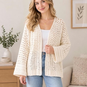 Può includere: Un cardigan color bianco sporco aperto sul davanti con un motivo a uncinetto dalla trama ariosa, maniche lunghe con polsini a coste e orlo dritto. Il capo è indossato sopra un top bianco semplice e un paio di jeans azzurri.