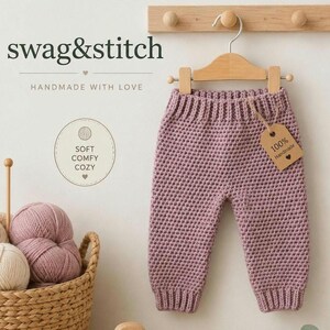 May include: Dusty rose crochet pants featuring a ribbed waistband and cuffs, hanging on a wooden hanger. A brown paper tag attached with twine reads 100% Handmade. Text on the image includes swag&stitch, HANDMADE WITH LOVE, and SOFT COMFY COZY.