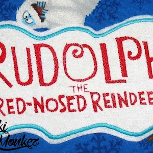 May include: A white patch with a blue border featuring the text "Rudolph the Red-Nosed Reindeer" in red lettering.