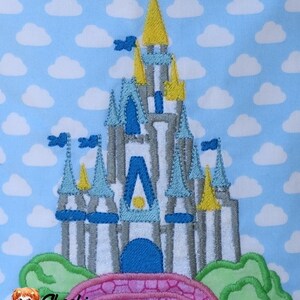 May include: Embroidered design of a light blue and gray castle with yellow and blue accents, set against a blue background with white clouds. The castle has a pink bridge in front of it.