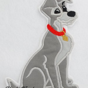 May include: A gray embroidered patch of a cartoon dog sitting with a red collar and a gold tag. The patch is on a white background.