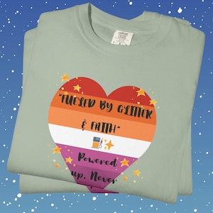 May include: A light green t-shirt with a heart-shaped graphic in orange, white, and purple. The graphic includes the text "Fueled by Glitter & Faith" and "Powered up. Never". The design is accented with yellow stars.