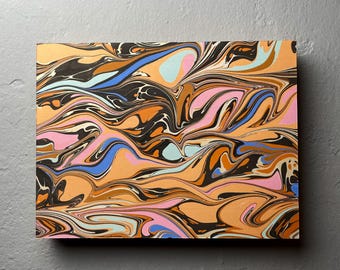 May include: Abstract art print featuring a swirling pattern in shades of orange, black, pink, blue, and light blue. The artwork has a marbled effect, creating a dynamic and colorful composition. The rectangular canvas is displayed against a gray background.