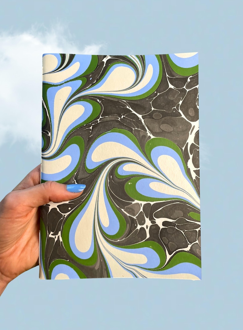 Puede incluir: Un cuaderno rectangular con una cubierta de papel jaspeado que presenta un patr&oacute;n de remolinos en colores crema, azul claro, verde bosque y gris carb&oacute;n. El dise&ntilde;o consiste en formas fluidas y org&aacute;nicas que crean un flujo visual continuo.