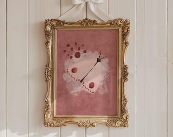 May include: A framed watercolor print of a butterfly in a gold ornate frame. The butterfly is light pink with dark pink spots and a black body. The frame is suspended by a white ribbon tied in a bow.