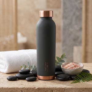 Könnte beinhalten: Eine matte anthrazitfarbene Wasserflasche mit einem metallischen kupferfarbenen Schraubverschluss und einem passenden kupferfarbenen Boden. Die Flasche trägt den vertikal aufgedruckten Text VELANTIC COPPER in einer dünnen, eleganten Schrift.