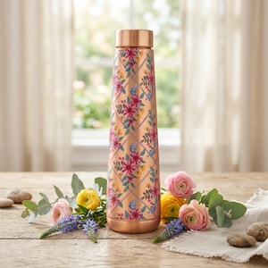 Könnte beinhalten: Eine zylindrische Wasserflasche aus Kupfer mit einem sich wiederholenden Rautenmuster, das mit farbenfrohen Blumenillustrationen in Rosa-, Lila- und Gelbtönen überlagert ist. Die Flasche hat eine glatte Metalloberfläche und einen passenden Schraubverschluss aus Kupfer.
