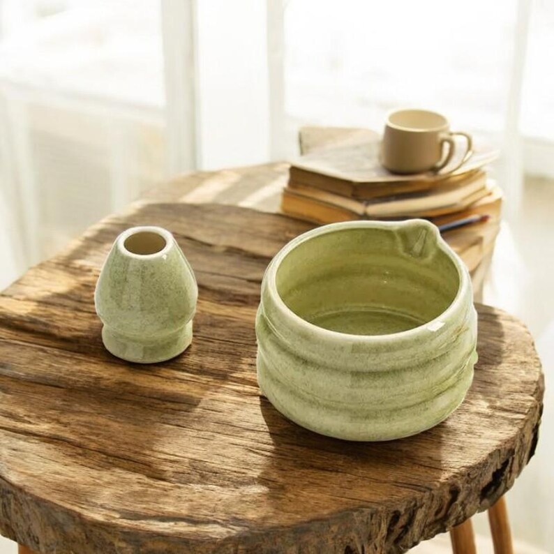 May include: Two green ceramic bowls, one larger than the other, with a textured, speckled finish. The bowls are sitting on a wooden table.