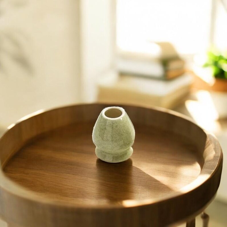 May include: A light green ceramic matcha whisk holder on a wooden tray. The holder has a rounded base and a wide opening at the top.